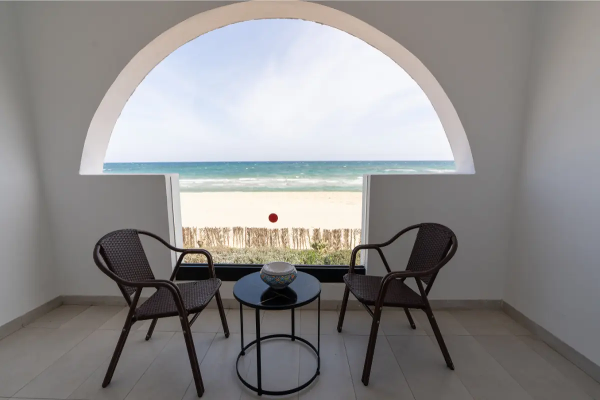 Terrasse privée avec vue directe sur la plage et la mer Méditerranée encadrée par une arche tunisienne à l'Hôtel Hammamet Beach, Hammamet Tunisie